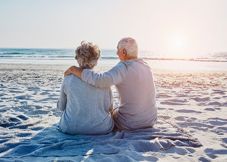 Senior couple sitting on the beach looking at distance